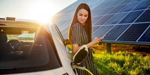 Woman waiting for electric car to charge and solar panels in background